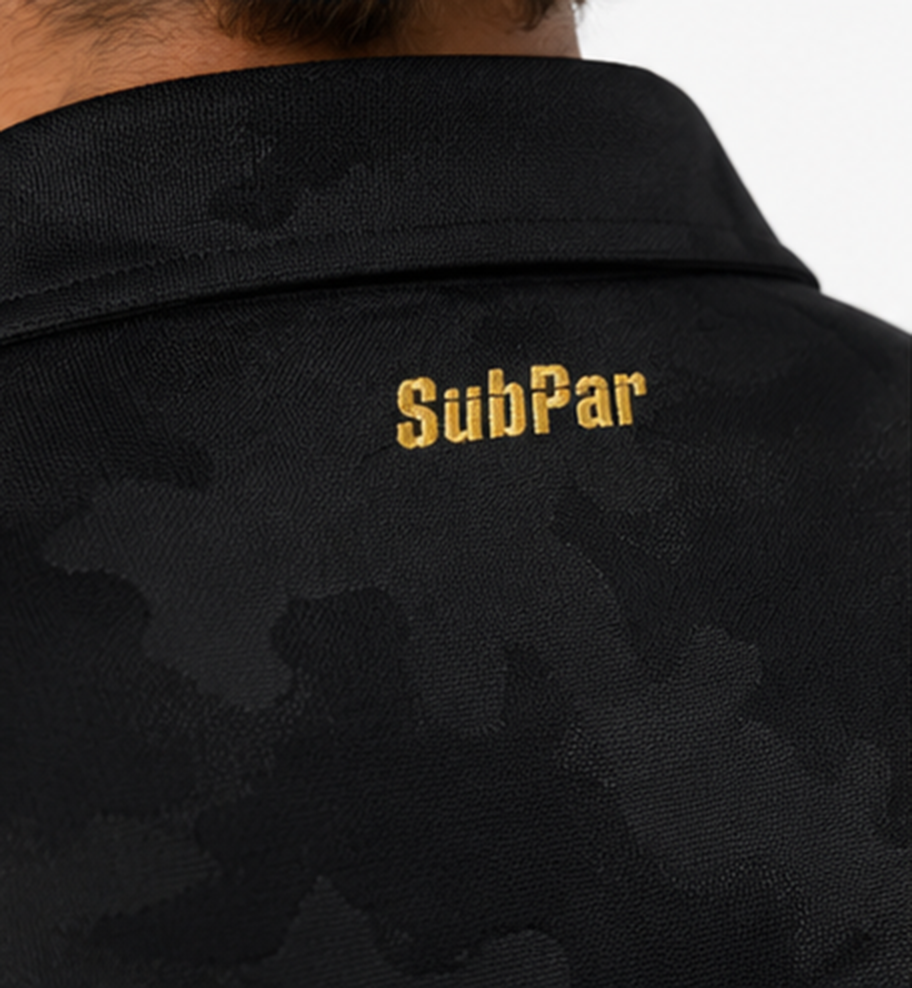 Close-up of the back of a black collared shirt with a subtle dark camouflage pattern and gold 'SubPar' embroidery on the collar.
